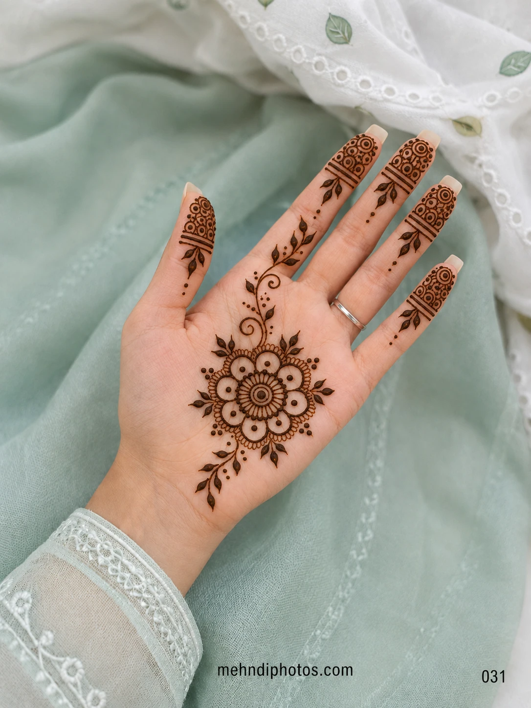 Front hand mehndi design featuring a layered floral mandala, leafy vines, curled details and circular patterns on the fingertips