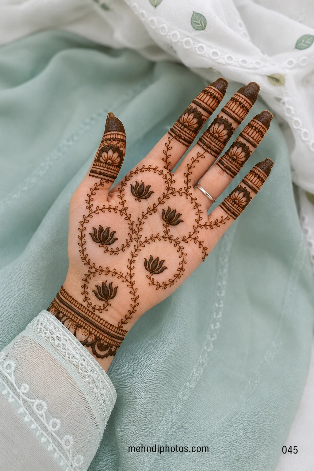 Front hand mehndi design featuring bold lotus motifs inside flowing leafy vines with floral finger panels and a decorative wrist border