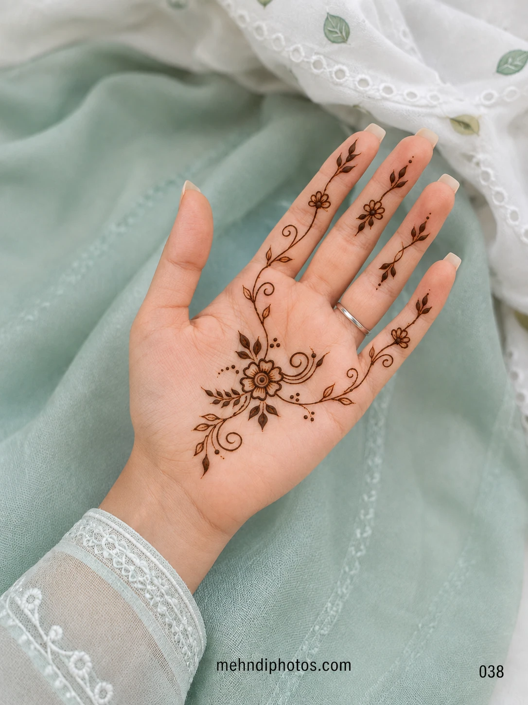 Minimal front hand mehndi design featuring a central flower with curling vines, delicate leaves and small floral accents on the fingers