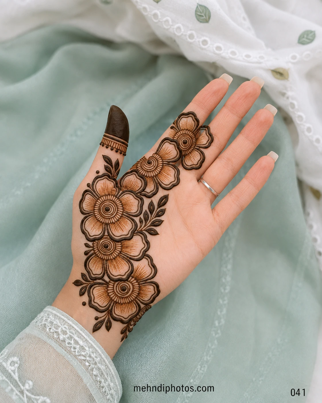 Front hand mehndi design featuring a diagonal trail of large shaded flowers with circular centres and dark leafy accents