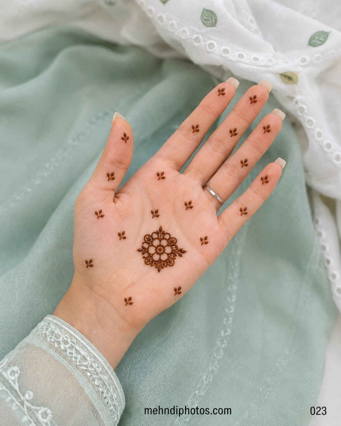 Minimal front hand mehndi design with a small floral tikki on the palm and tiny leafy motifs across the fingers