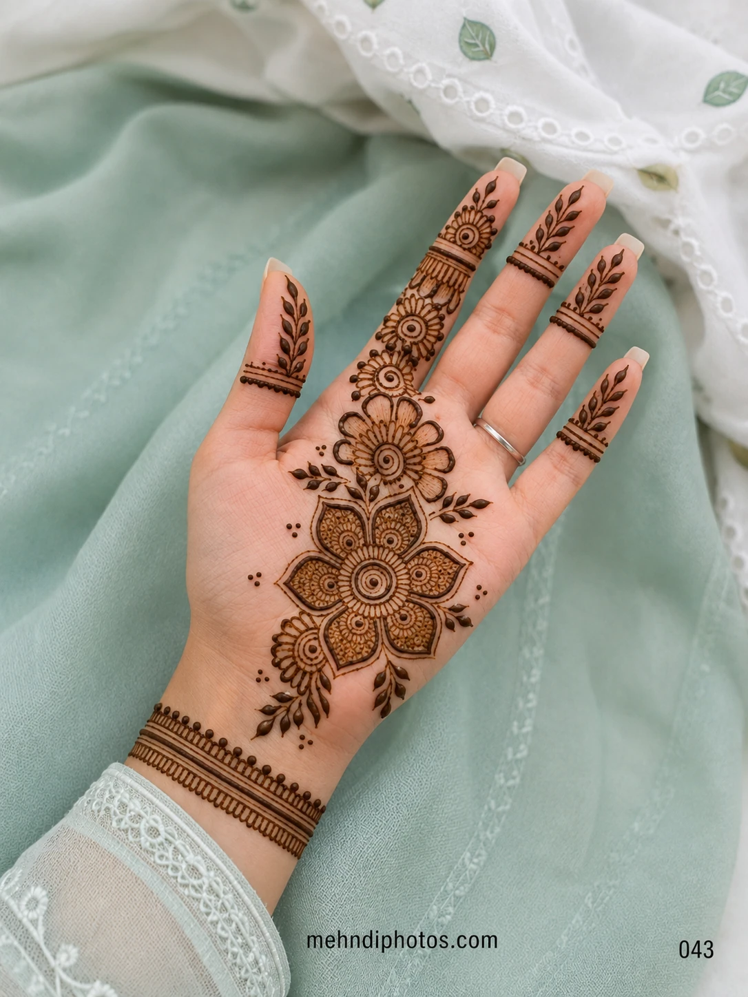 Front hand mehndi design featuring a large layered flower, smaller blossoms, leafy branches, finger motifs and a bracelet-style wrist band