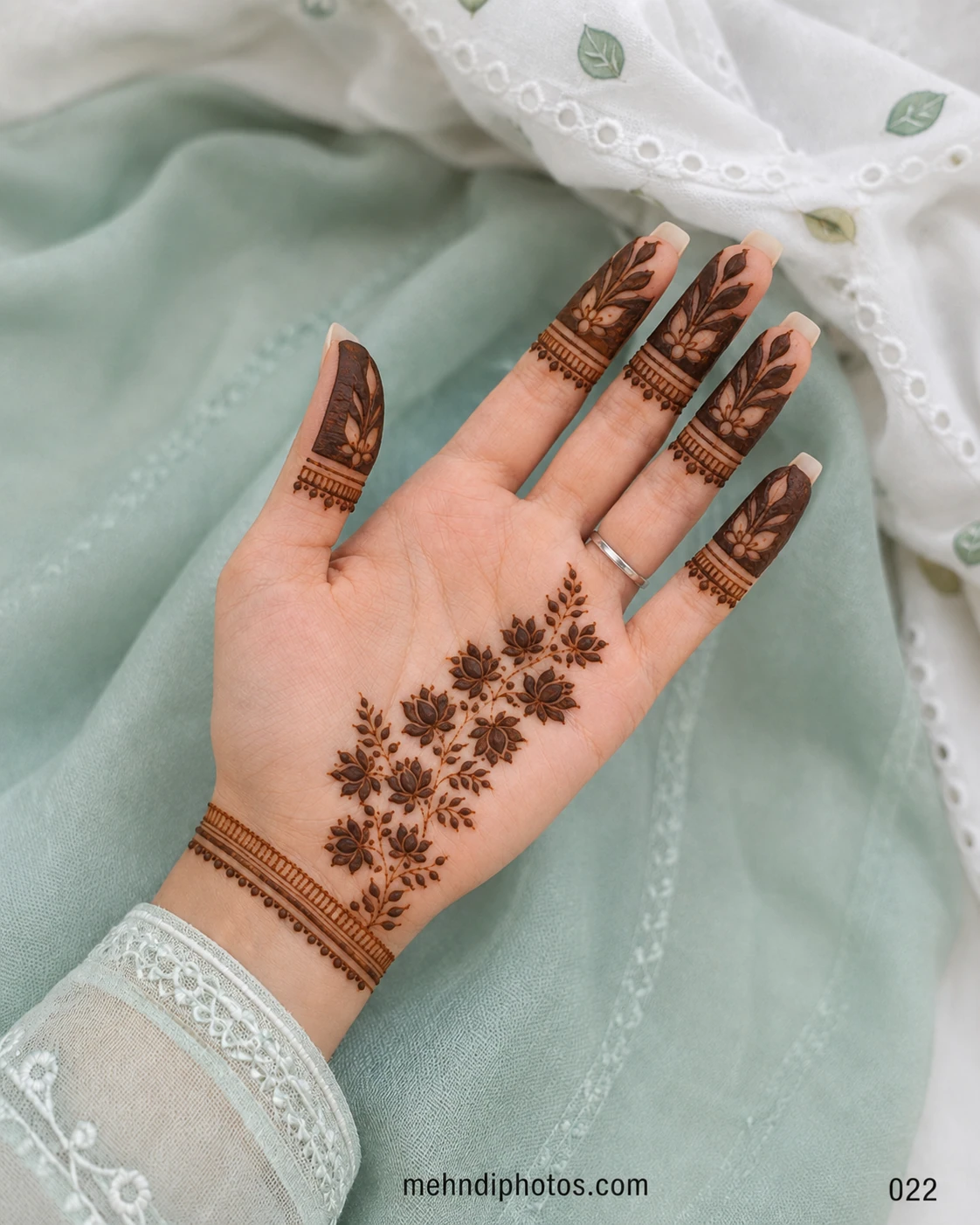 Front hand mehndi design featuring a diagonal floral vine, leafy fingertips and fine band patterns around the wrist