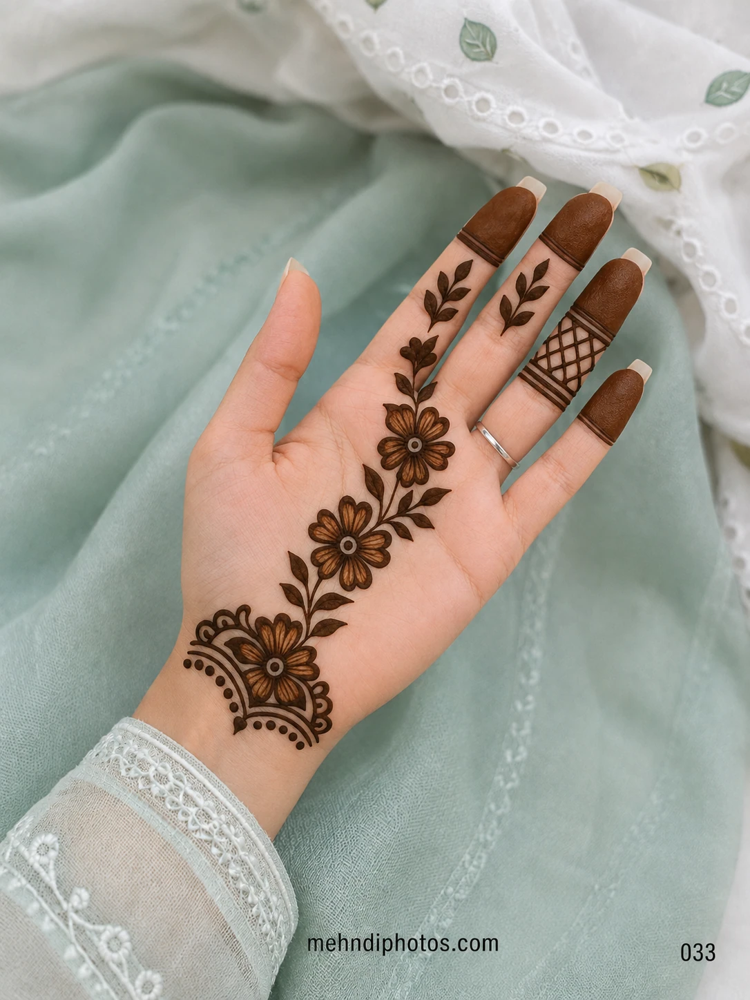 Front hand mehndi design with a diagonal Arabic floral vine, shaded flowers, dark leaves, filled fingertips and a lattice finger accent