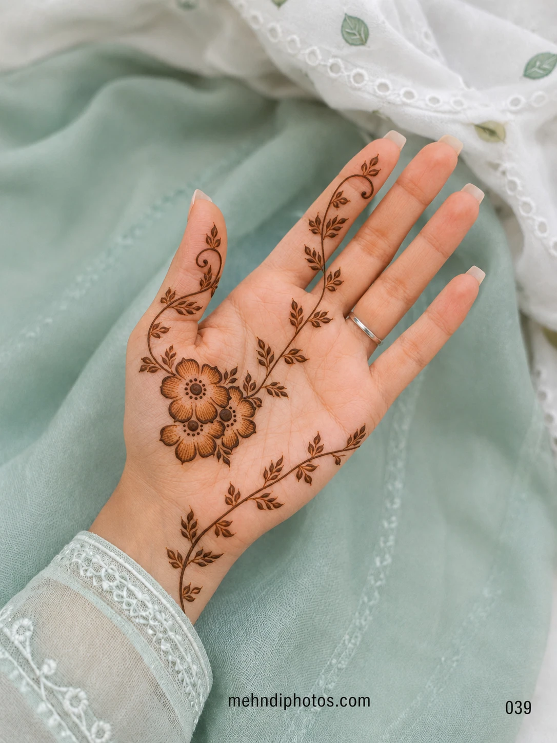 Front hand mehndi design featuring three shaded flowers with long flowing leafy vines extending across the palm, wrist and fingers