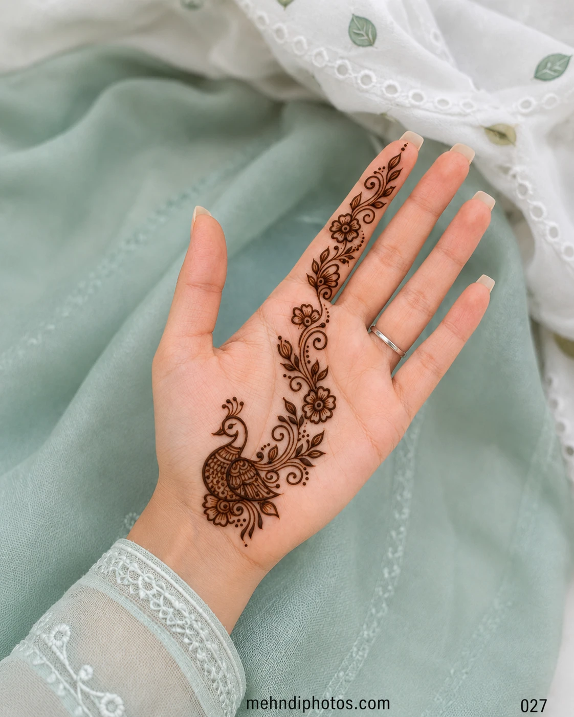 Front hand mehndi design with a detailed peacock near the wrist and a floral vine extending across the palm and index finger