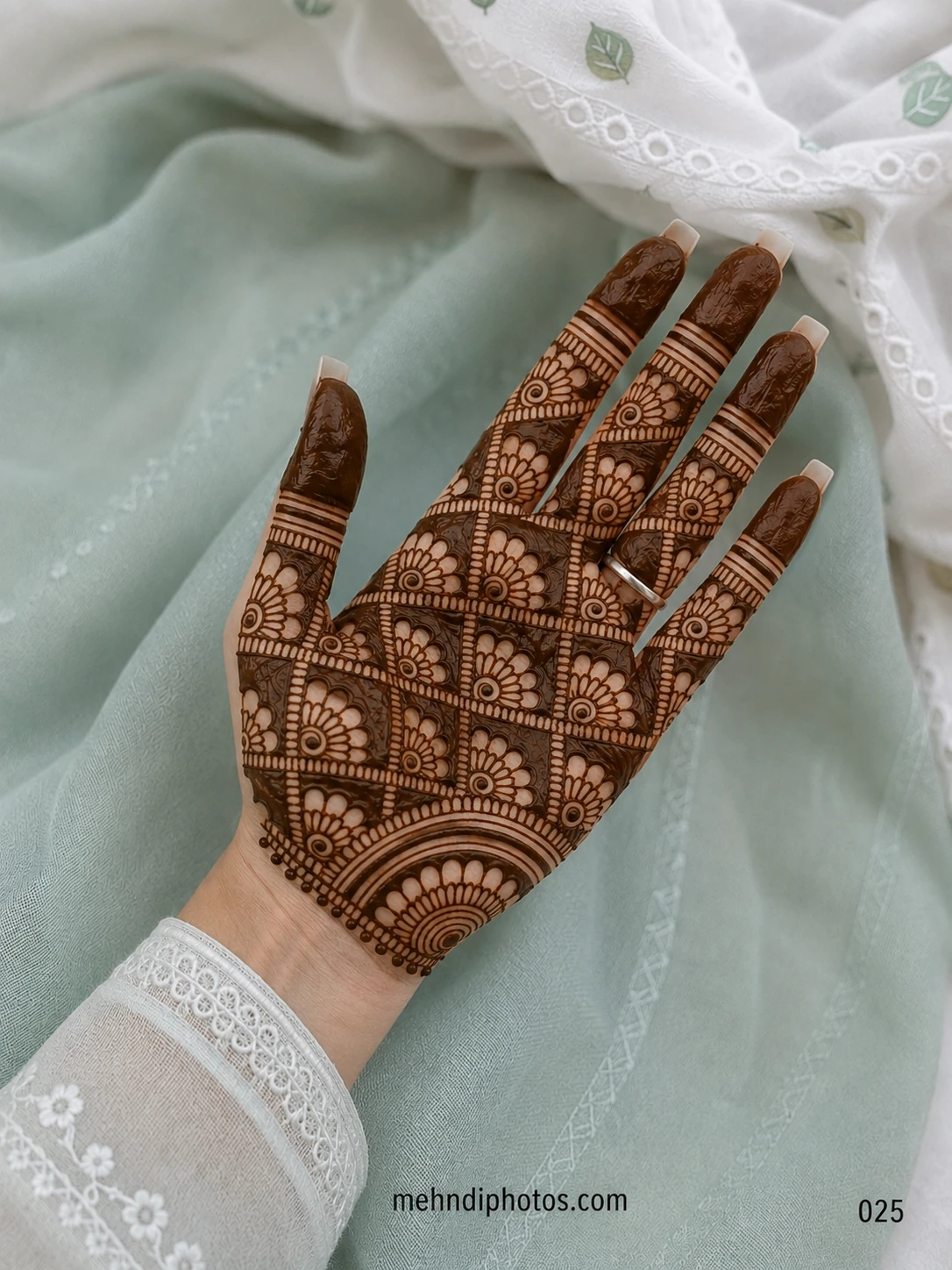 Full front hand mehndi design featuring a floral grid pattern, dark shaded sections, bold fingertips and a semicircular wrist motif