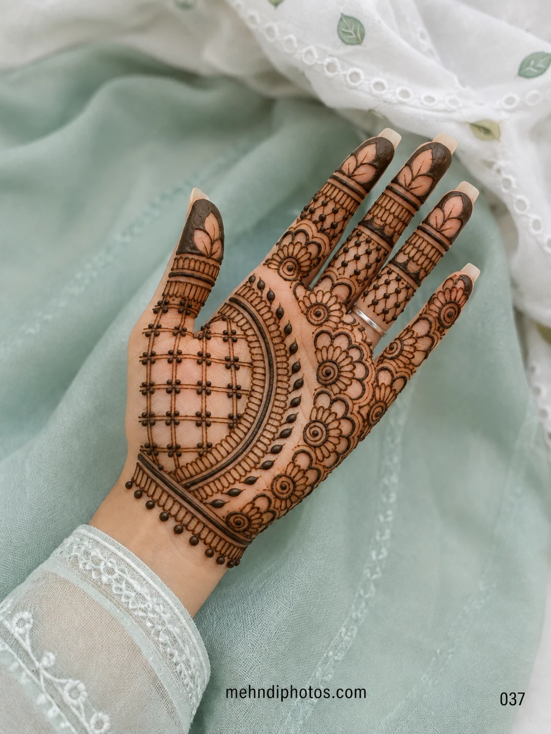 Detailed front hand mehndi design featuring a curved lattice pattern, floral borders, leafy accents and dark fingertips with open leaf shapes