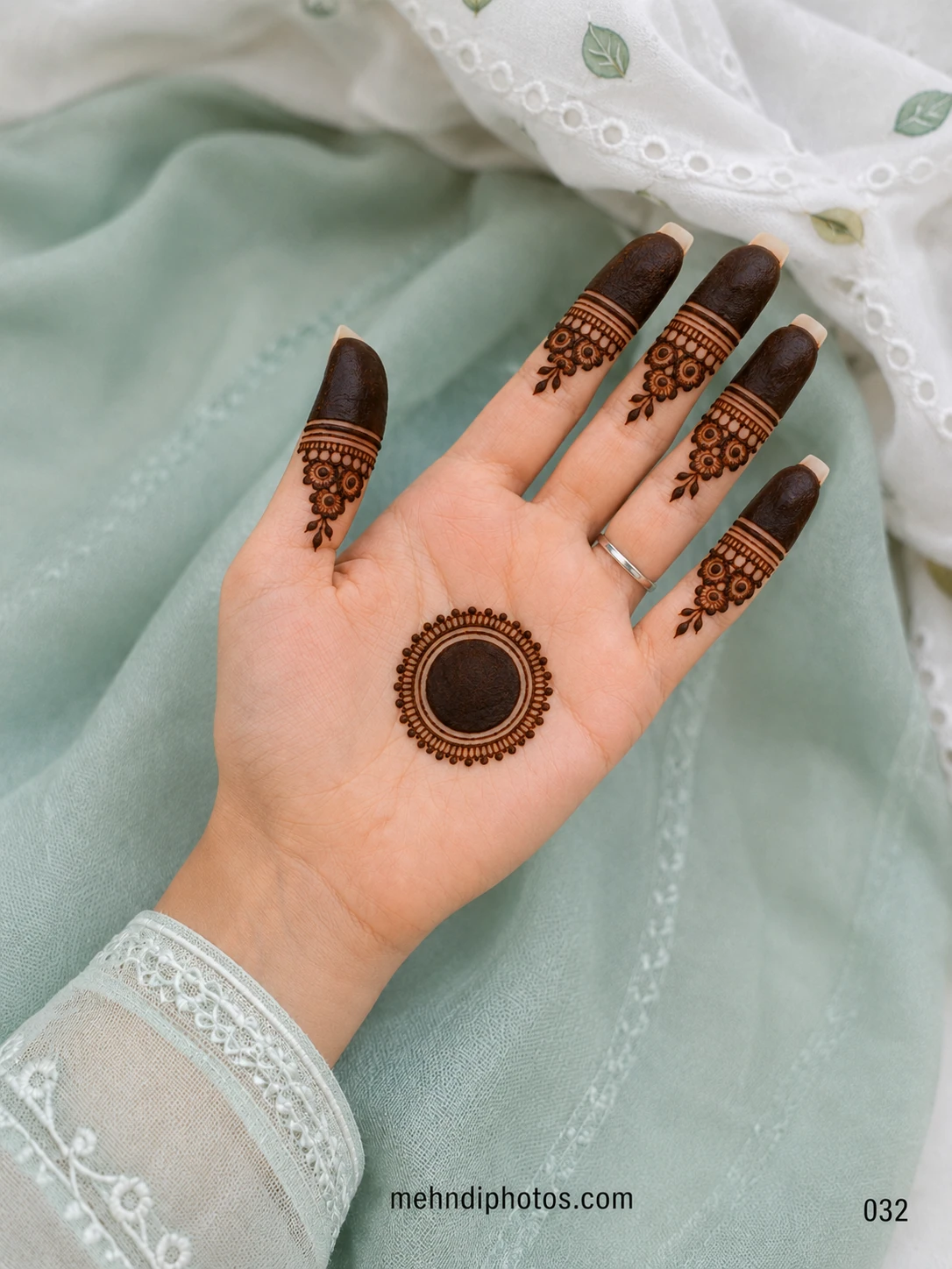 Front hand mehndi design with a bold circular gol tikki on the palm, dark fingertips and small floral finger patterns