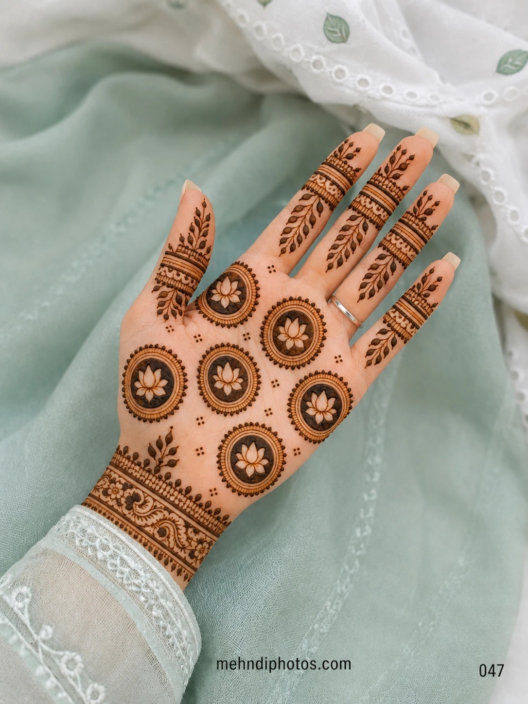 Front hand mehndi design featuring circular lotus medallions across the palm, leafy finger trails and an ornamental paisley wrist border