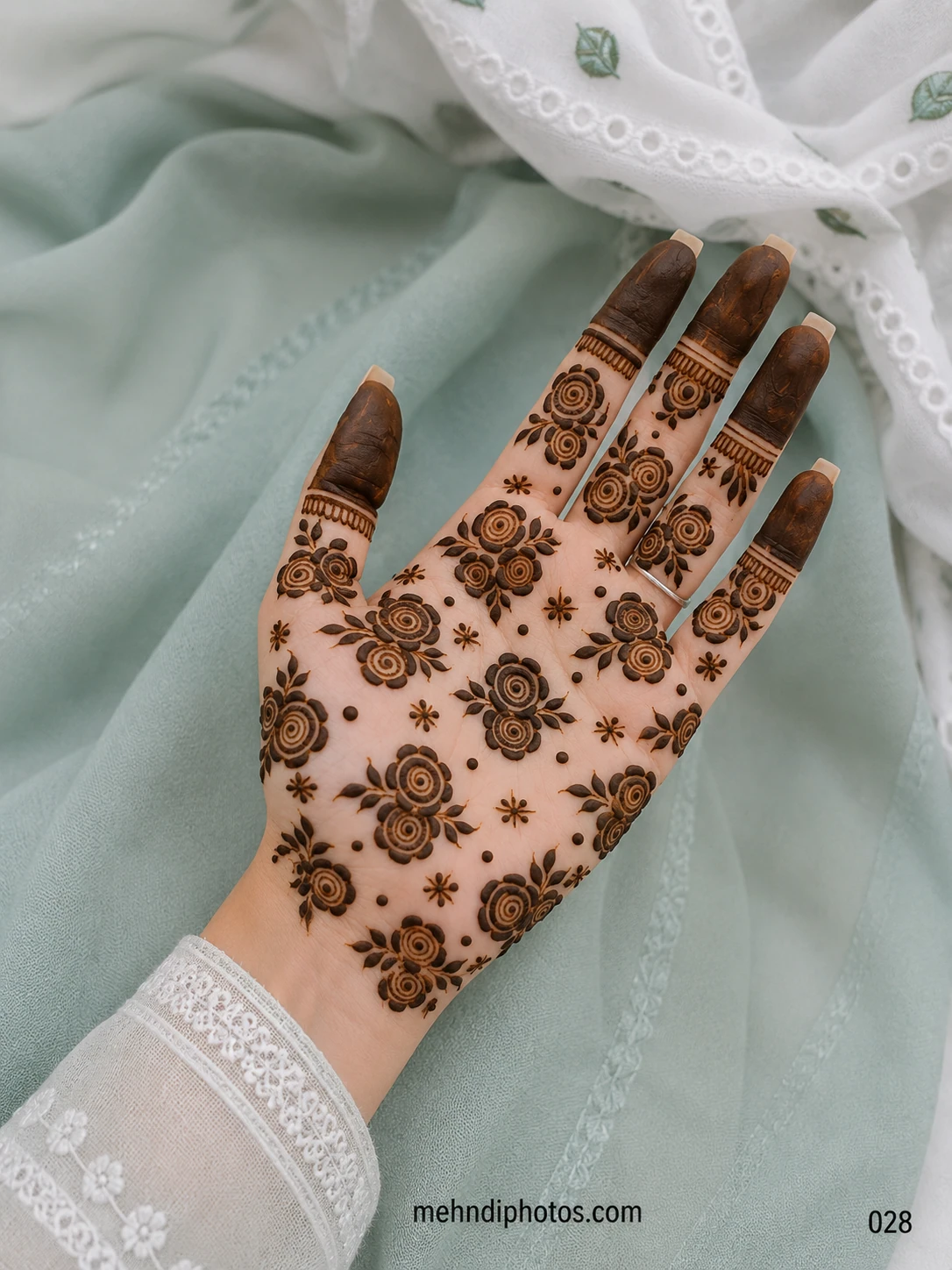 Front hand mehndi design featuring bold spiral roses, small leafy accents, dotted details and darkly filled fingertips