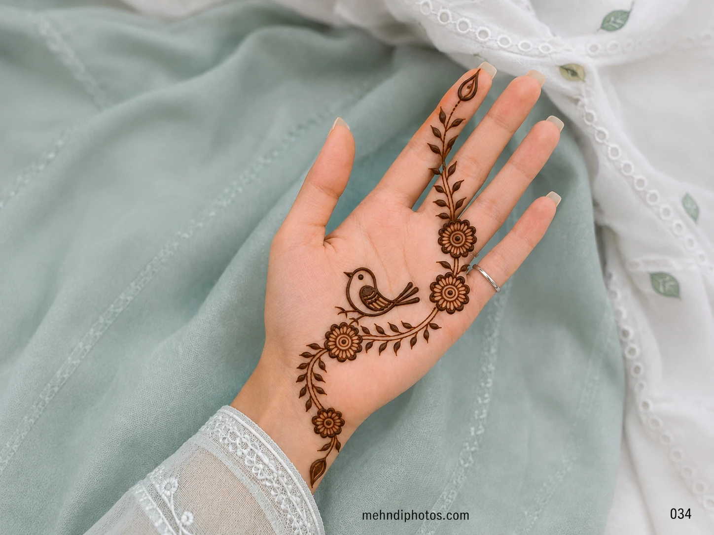 Front hand mehndi design featuring a small bird surrounded by rounded flowers and a flowing leafy vine from the wrist to one finger