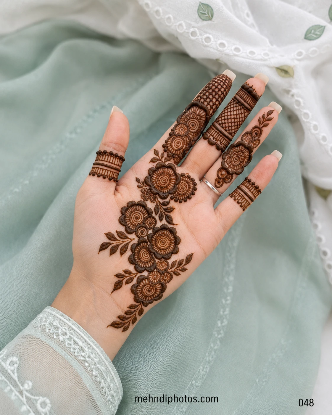 Front hand mehndi design featuring a diagonal trail of layered flowers and leaves with lattice panels and ornamental bands on the fingers