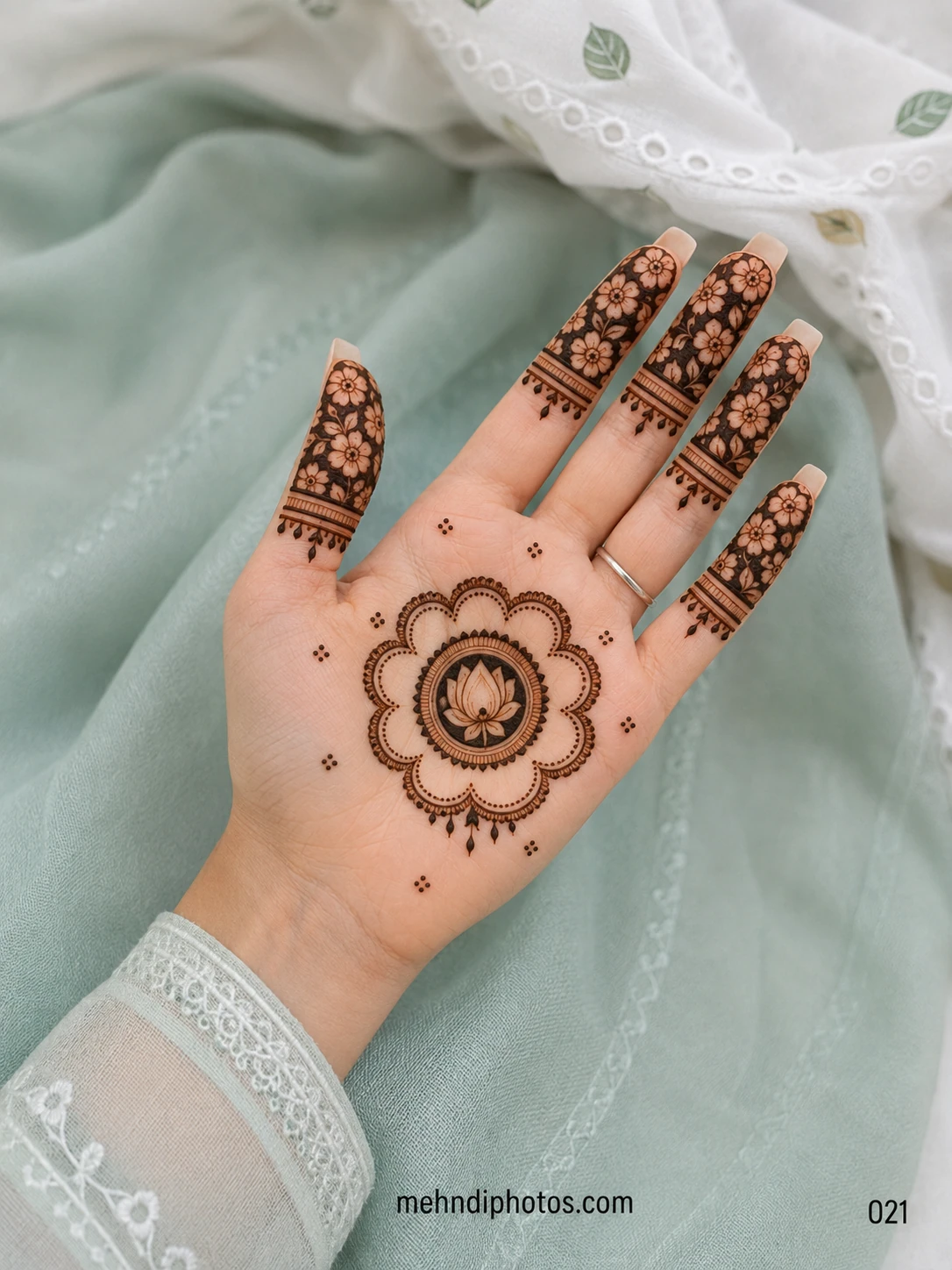 Front hand mehndi design with a lotus mandala on the palm and dark floral patterns covering the fingers