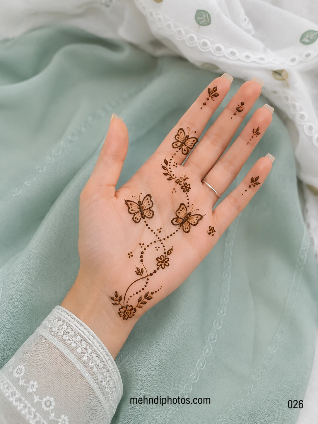 Minimal front hand mehndi design featuring three butterflies, dotted trails, small flowers and delicate leafy vines