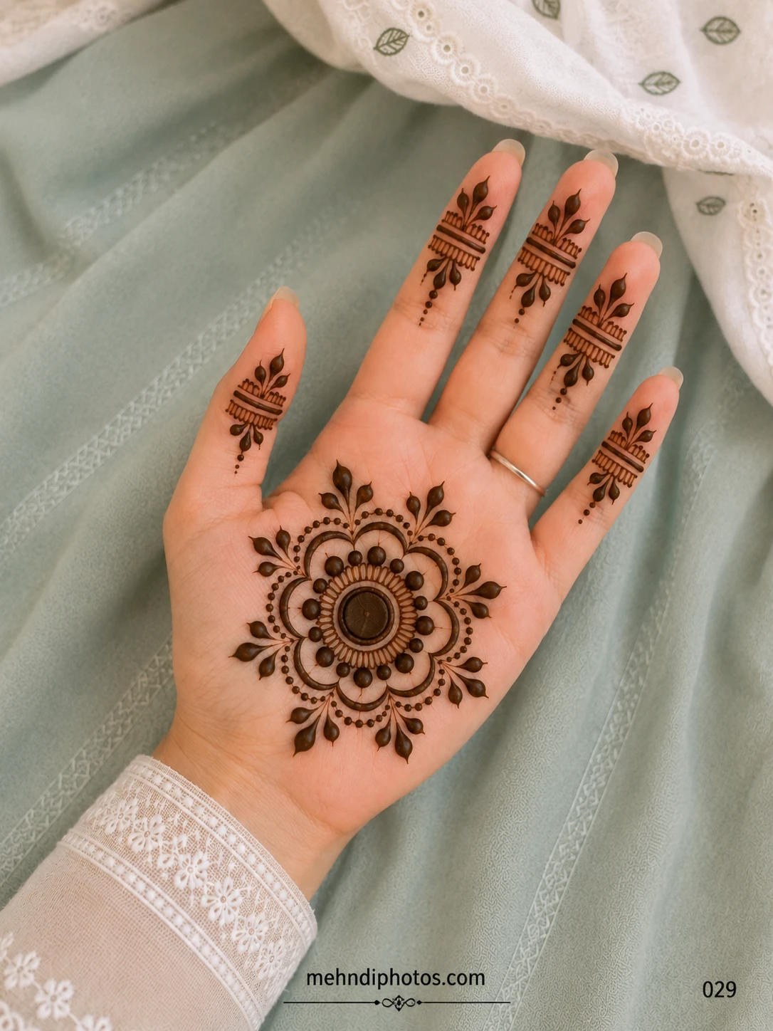 Front hand mehndi design with a bold floral mandala on the palm and matching leafy band patterns on each finger