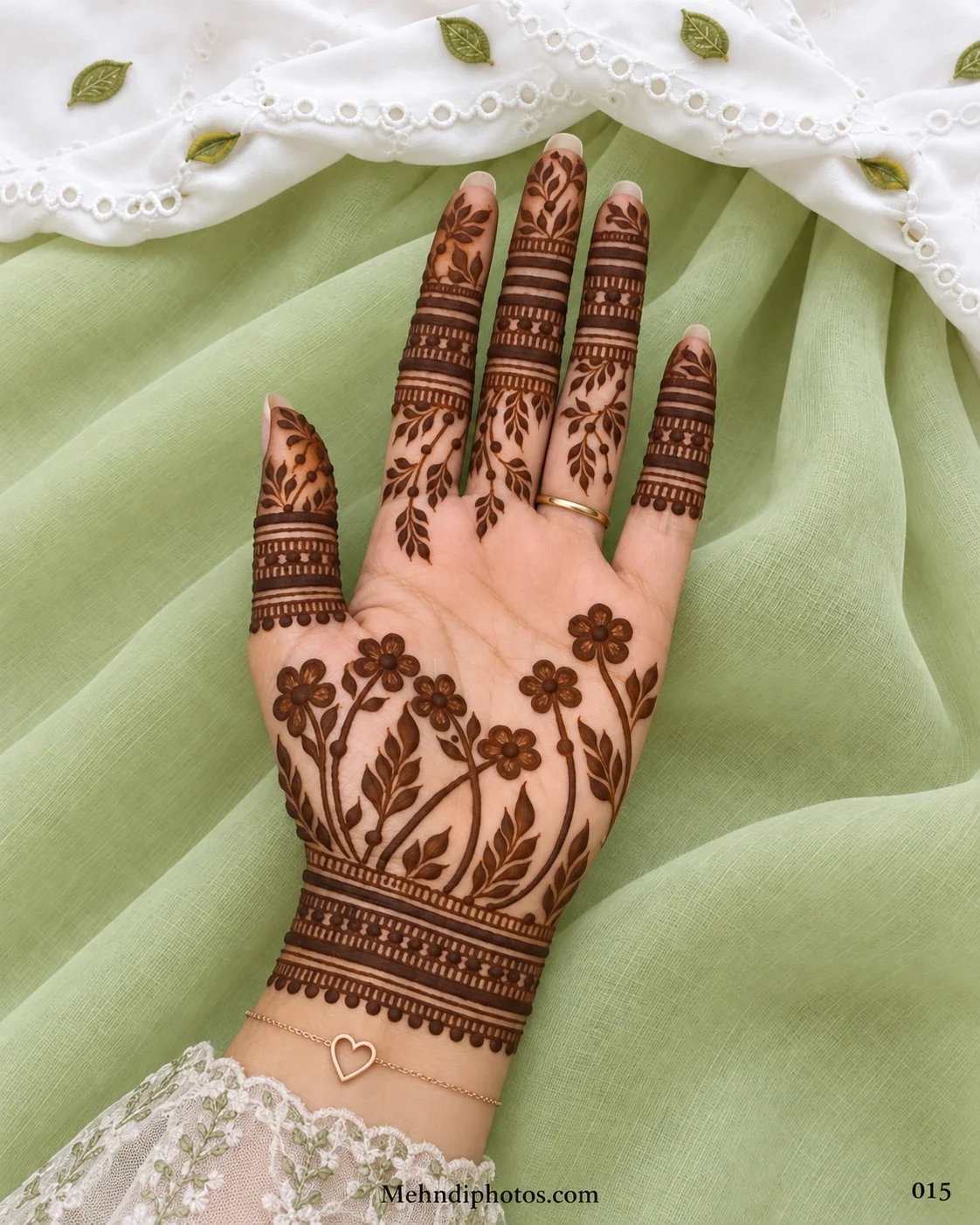 Front hand mehndi design with garden flowers, curved leafy branches, bold finger bands, hanging dots, and a decorative wrist border.
