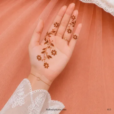 Front hand with a delicate diagonal floral vine, shaded leaves, curling stems and small daisy mehndi motifs on the palm and fingers.