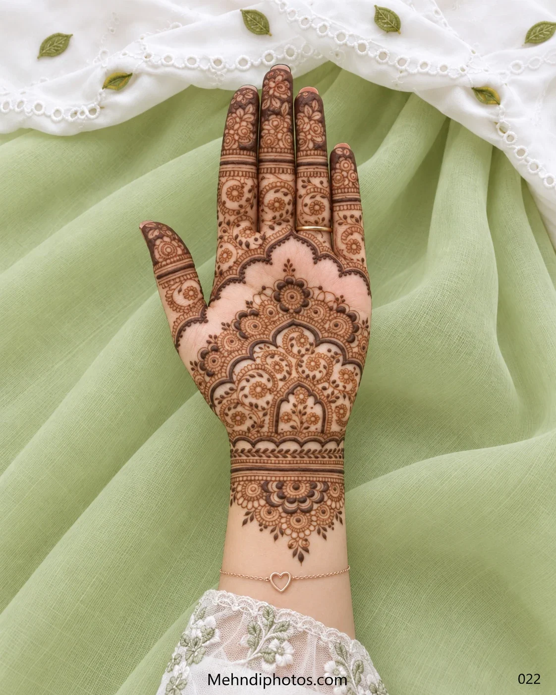 Front hand mehndi design with layered floral arches, circular motifs, scalloped borders, decorated fingertips, and an ornamental wrist pattern.
