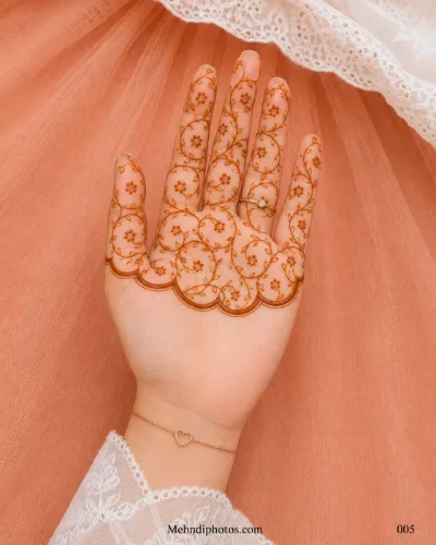 Front hand with looping floral vines across the fingers and upper palm, finished with a bold scalloped mehndi border.