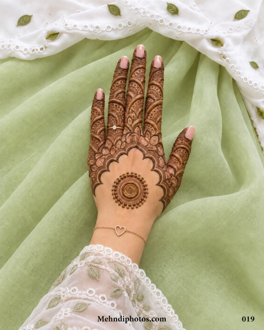 Back hand mehndi design with a small circular mandala, open scalloped border, dense paisley arches, teardrop motifs, and decorated fingers.