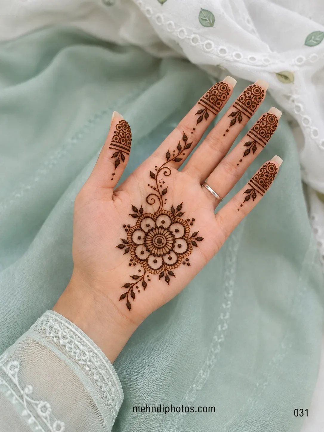 Front hand mehndi design featuring a layered floral mandala, leafy vines, curled details and circular patterns on the fingertips