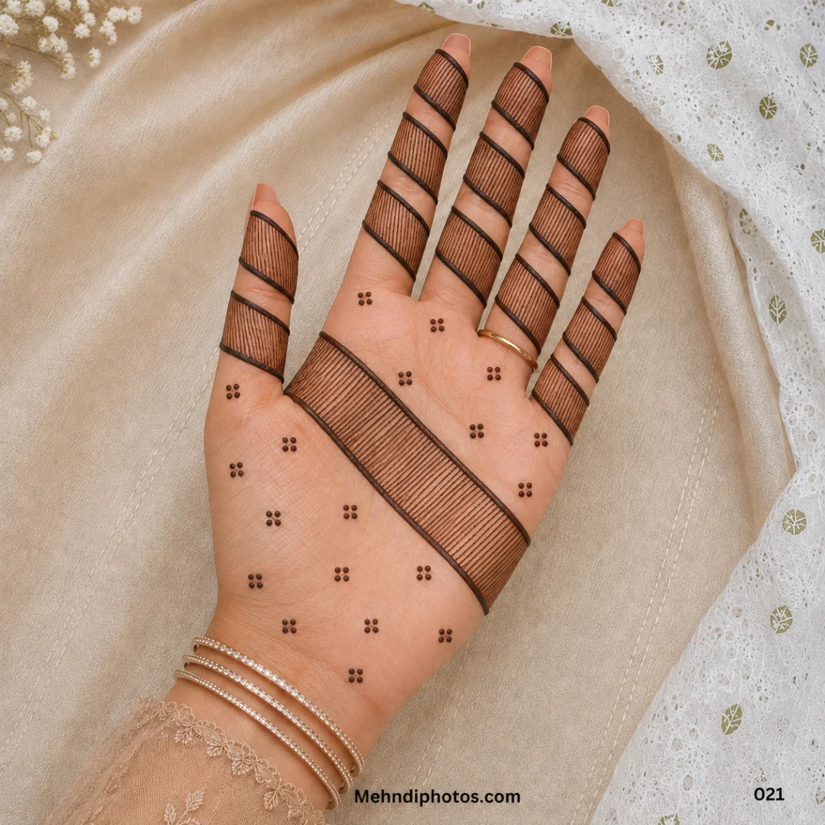 Front hand with fine striped mehndi enclosed in bold diagonal bands across the fingers and palm, finished with small dot clusters.