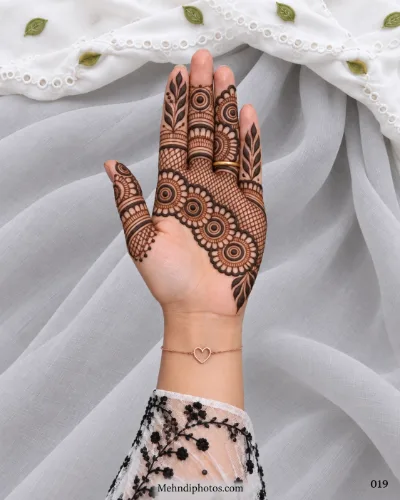 Eid front hand mehndi featuring a diagonal row of circular flowers, fine net filling, leafy finger motifs, geometric bands, and open palm space.