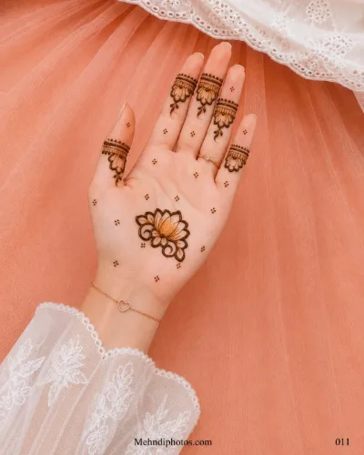 Front hand with a central lotus mehndi motif, hanging floral finger bands and small dot clusters across the open palm.
