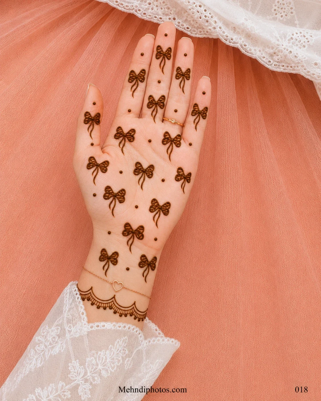 Front hand decorated with small bow mehndi motifs, scattered dots and a delicate scalloped border with hanging details near the wrist.