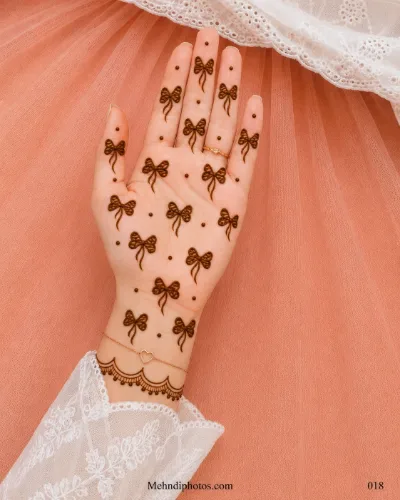 Front hand decorated with small bow mehndi motifs, scattered dots and a delicate scalloped border with hanging details near the wrist.