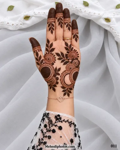 Eid front hand mehndi featuring bold circular flowers with spiral centers, leafy branches, open rings, and dark decorated fingertips.