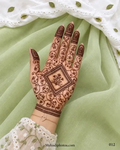Front hand mehndi design with a square floral centerpiece, curling leafy vines, layered fingertip arches, and a striped wrist border.
