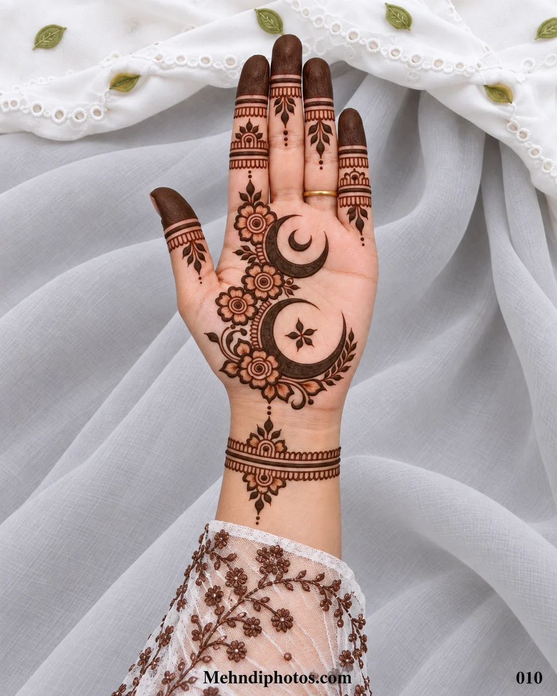 Eid front hand mehndi featuring two crescent moons connected by flowers and leafy vines with dark fingertips and a floral wrist band.
