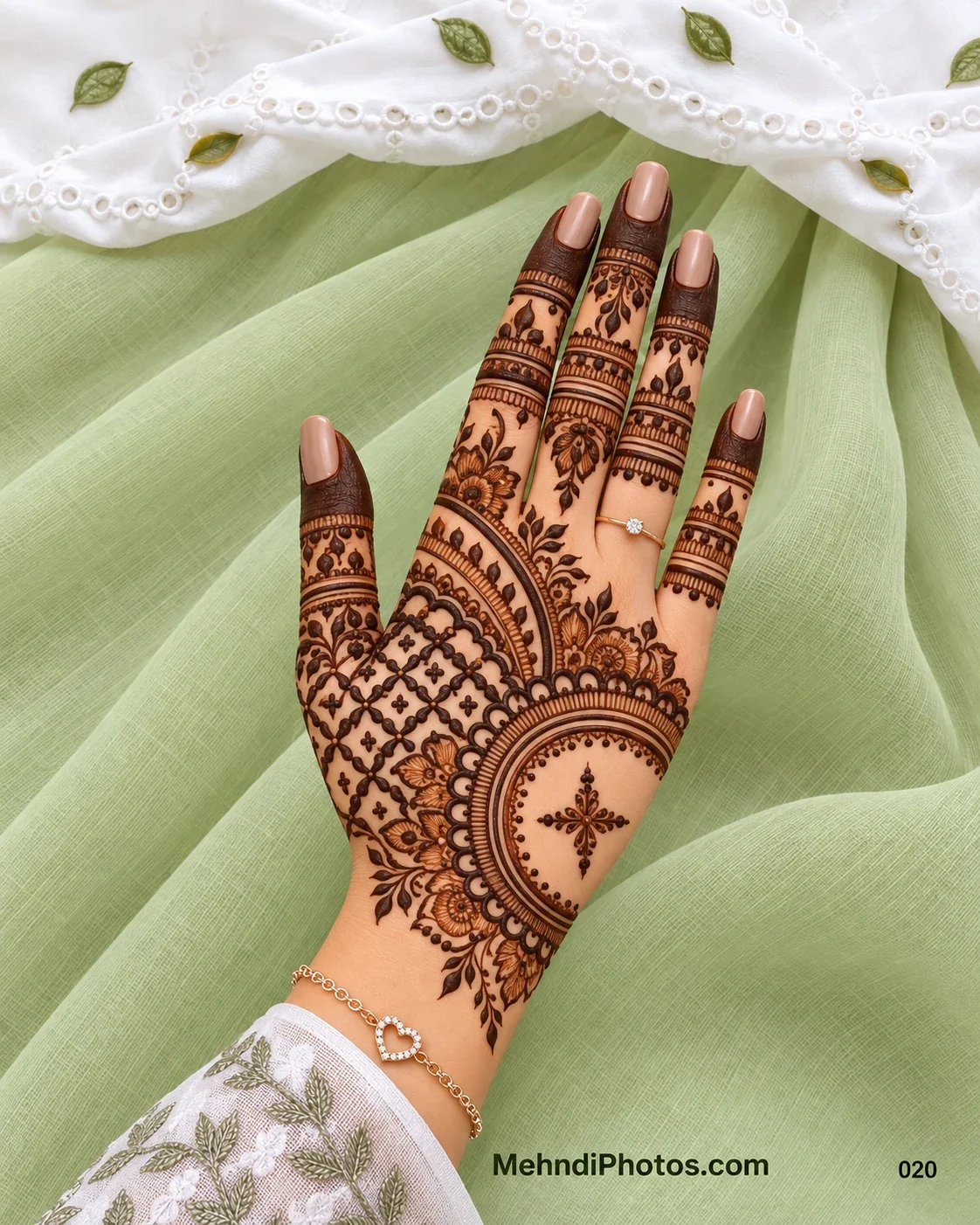 Back hand mehndi design with a circular floral frame, four-point center motif, scalloped borders, latticework, leafy vines, and finger bands.