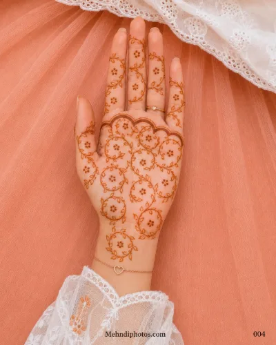 Front hand decorated with circular leafy mehndi vines, tiny dot flowers and a scalloped border across the upper palm.