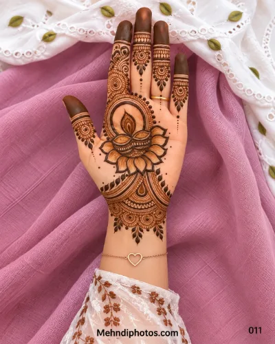 Diwali front hand mehndi design with a shaded diya on lotus petals, circular mandala frame, sunburst finger motifs, dark tips, and an ornate wrist.