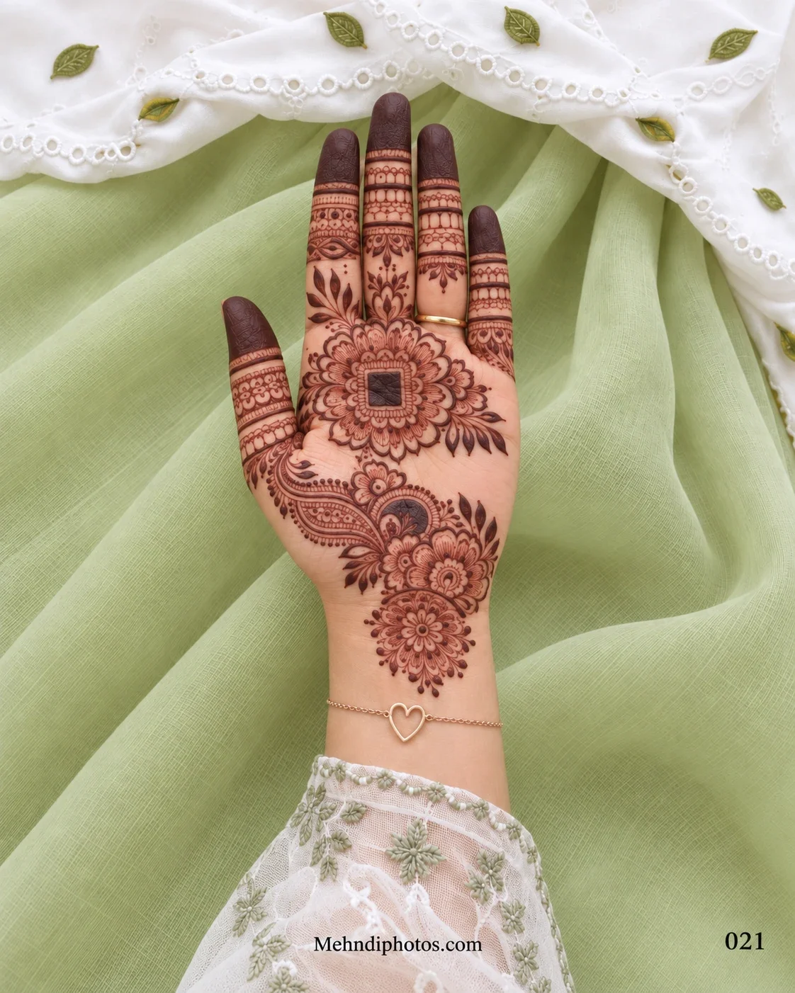 Front hand mehndi design with a layered floral mandala, bold square center, paisley flower trail, decorative finger bands, and shaded fingertips.