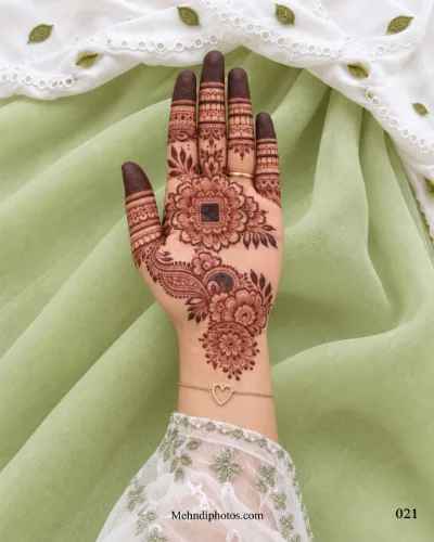 Front hand mehndi design with a layered floral mandala, bold square center, paisley flower trail, decorative finger bands, and shaded fingertips.